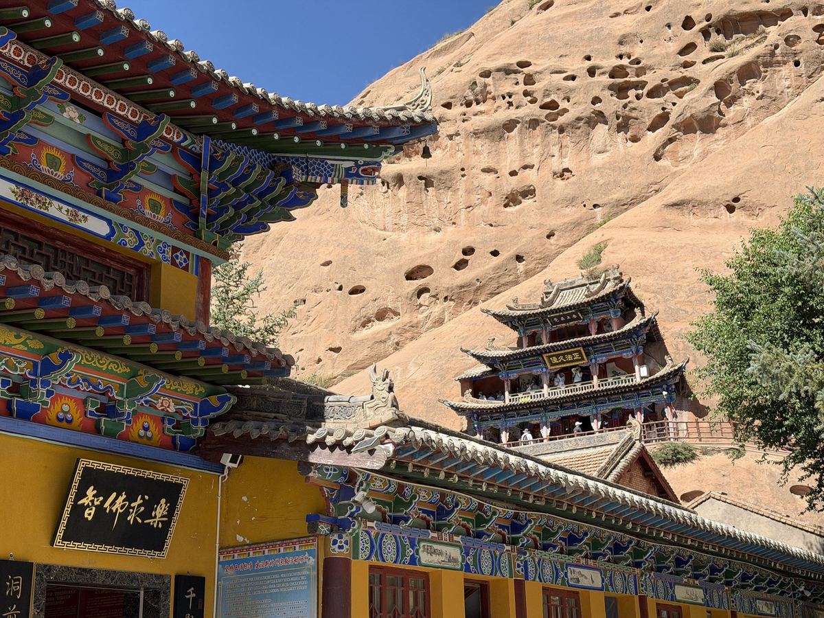 Painted eaves of the Thousand Buddha Caves temple with a three storey pavilion set into the cliff behind, Mati Temple
