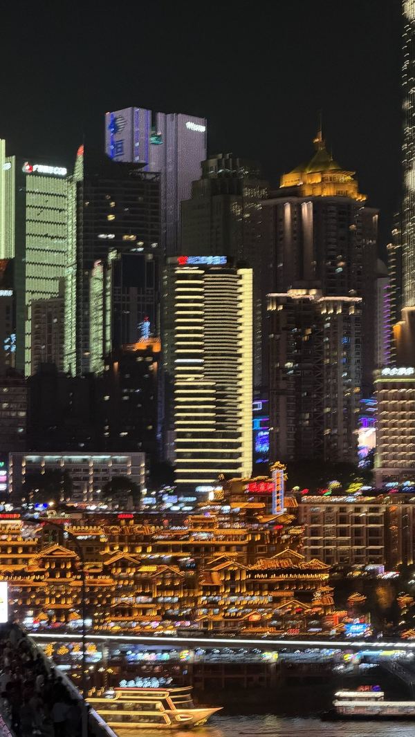 Hongyadong stilt houses lit gold at night below Chongqing skyscrapers