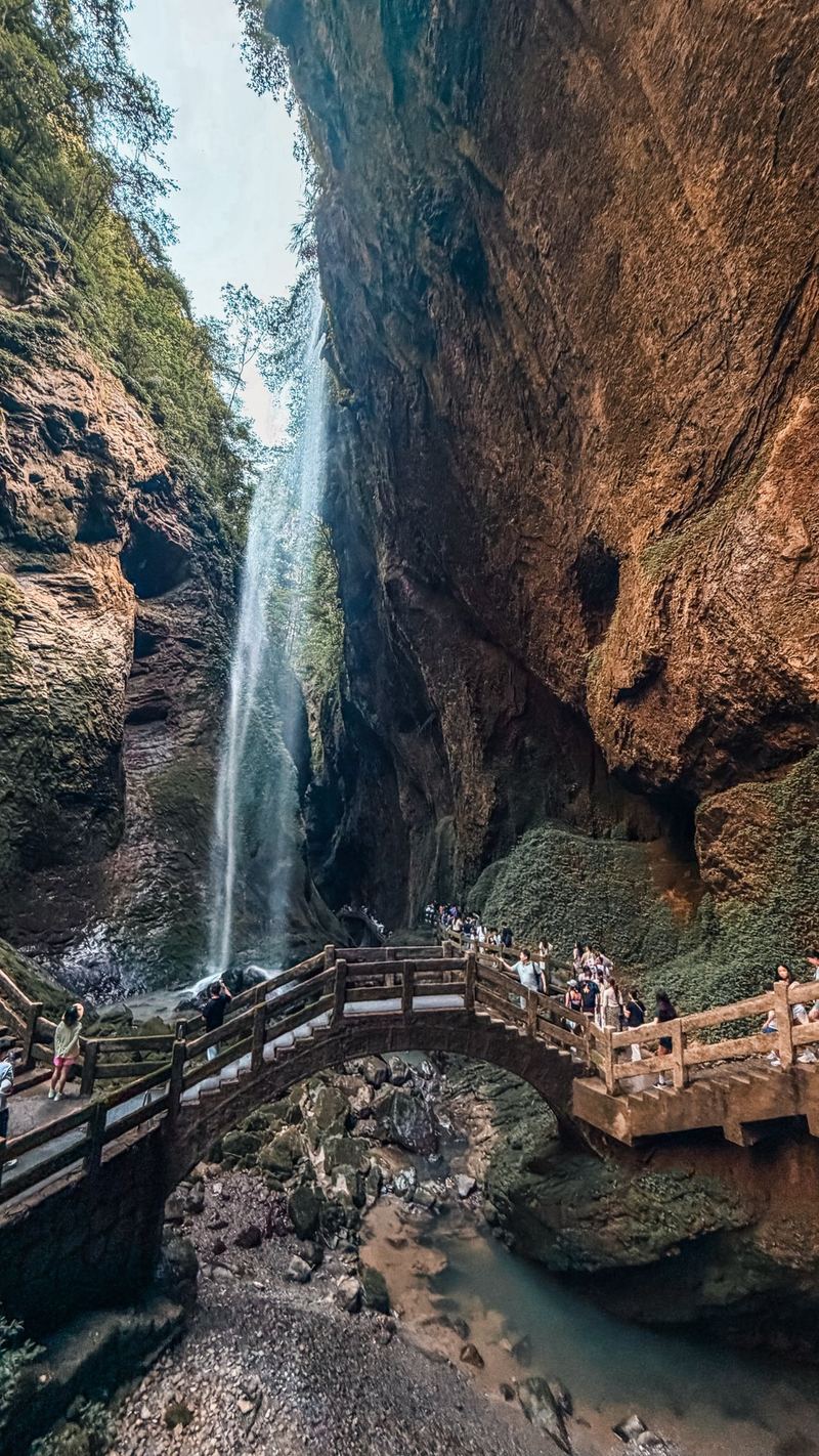 An arched stone bridge below a tall waterfall in Longshuixia gorge, Wulong