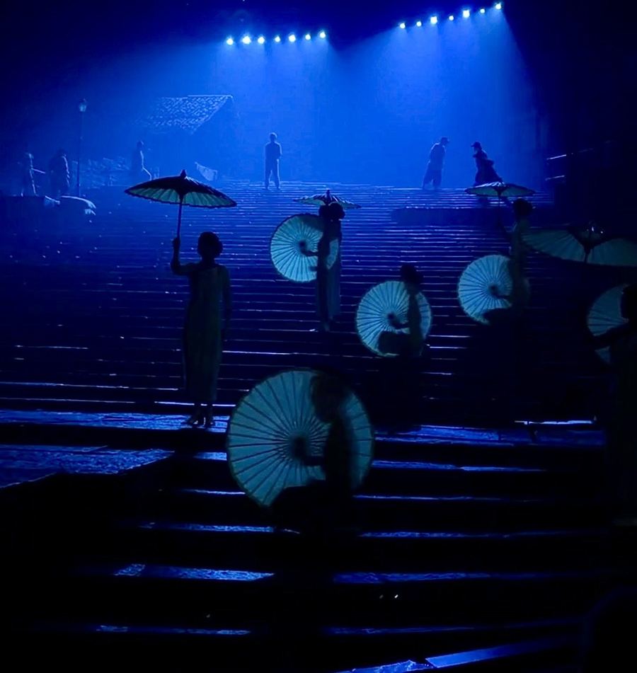 Dancers with paper umbrellas on a blue-lit staircase in the Chongqing 1949 show