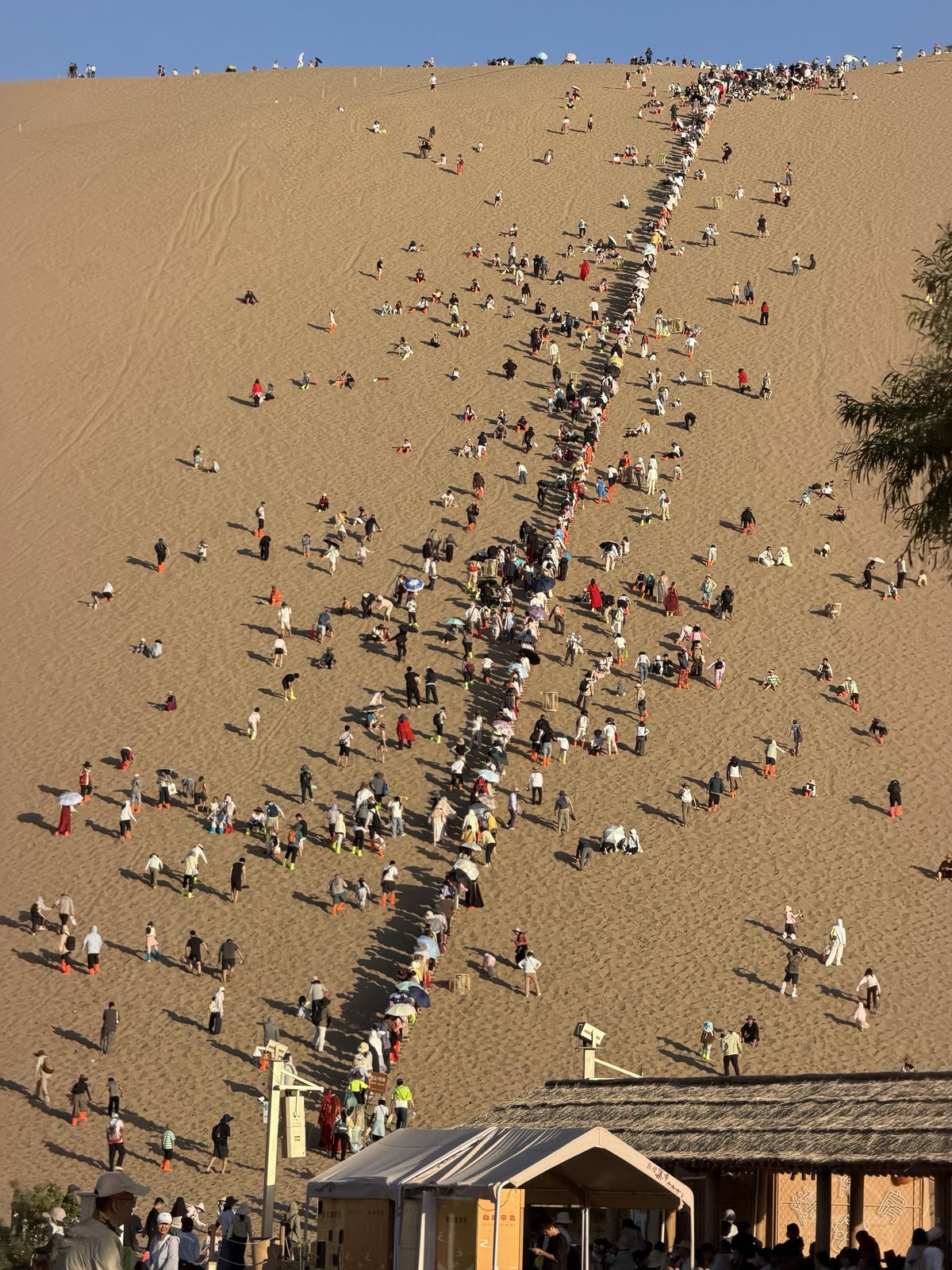 Visitors in orange sand shoe covers climbing the Mingsha Shan dune, Dunhuang