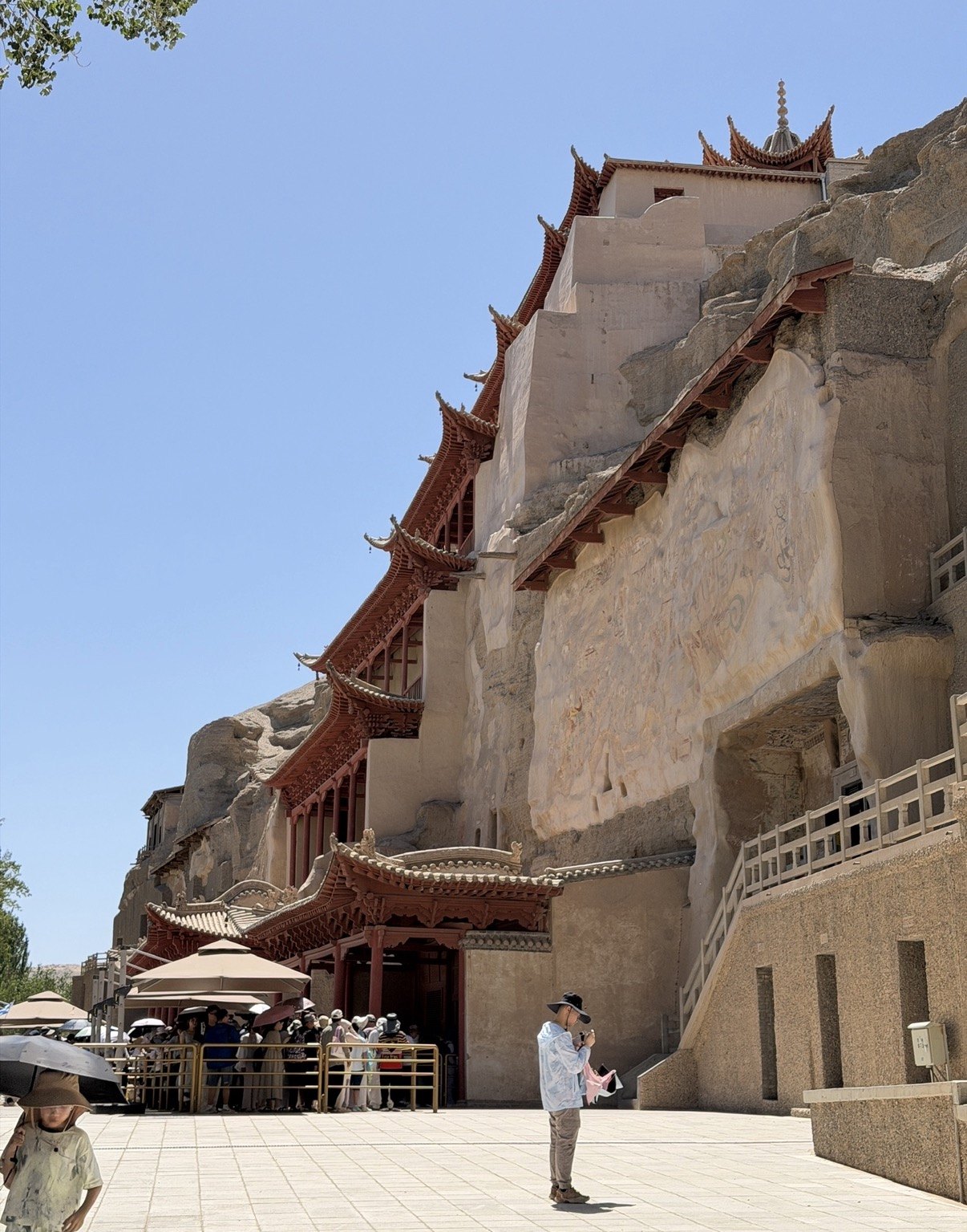 Visitors queuing below the red eaves and cliff face of the Mogao Caves on a sunny day