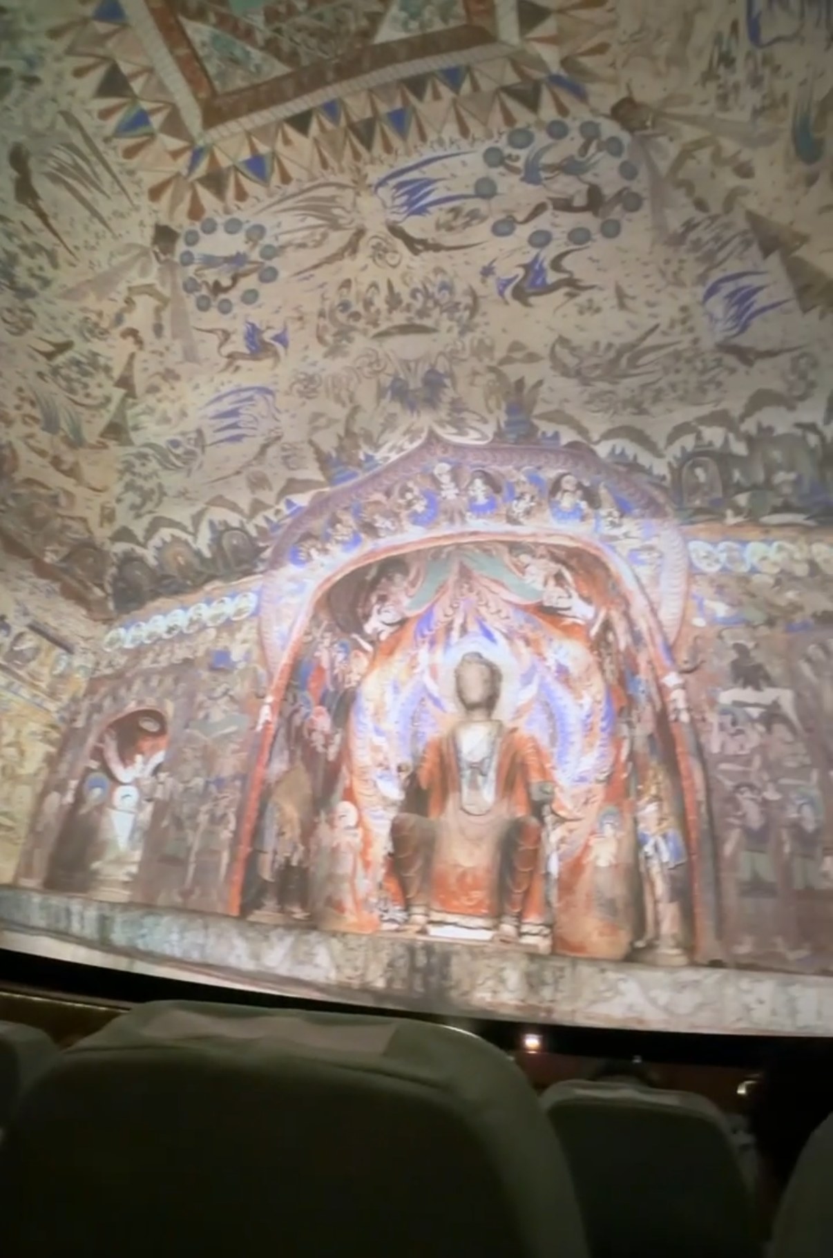 A seated Buddha in a painted niche, projected in the dome theatre at the Mogao visitor centre