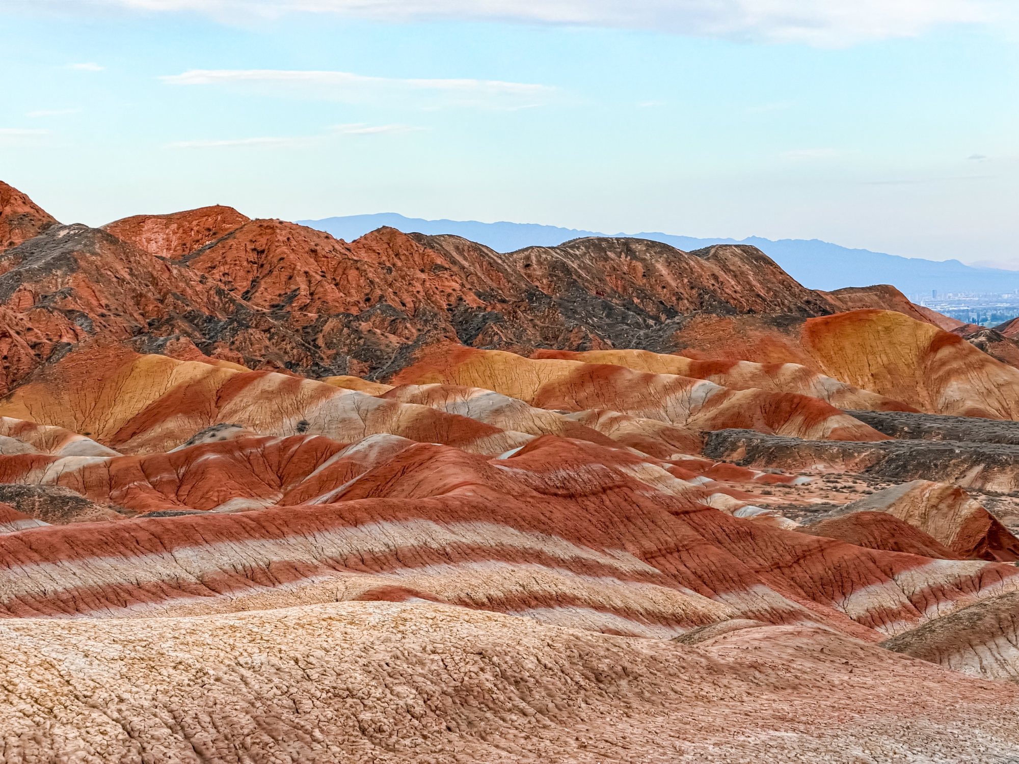 Waves of red and white striped hills in the Zhangye Danxia, mountains in the distance